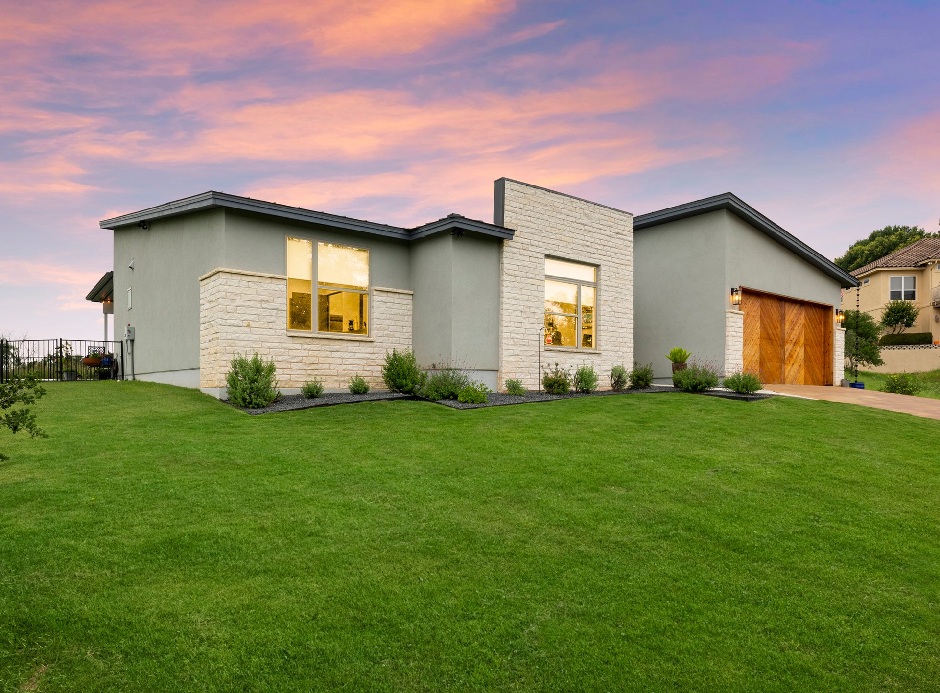 Modern single-story house with a lush green lawn at sunset.
