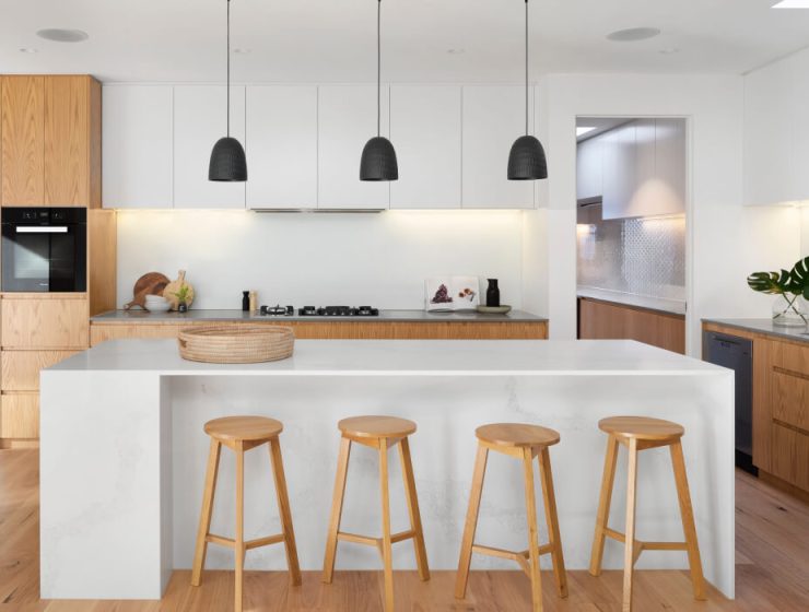 Modern kitchen with wooden stools and pendant lights.