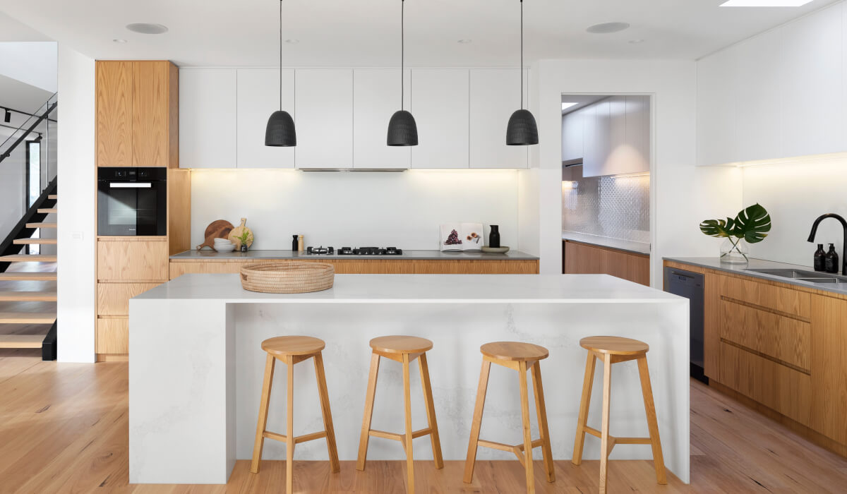 Modern kitchen with wooden stools and pendant lights.