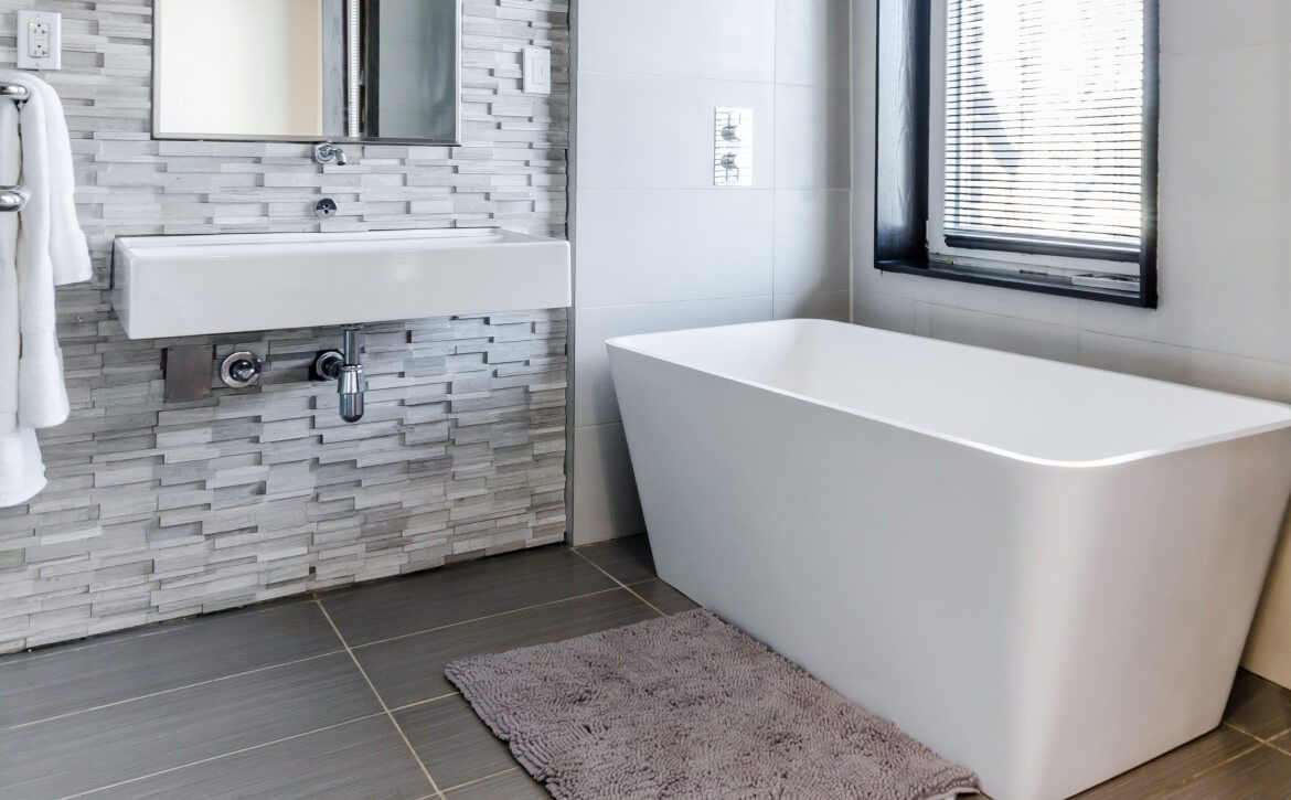Modern bathroom with a white bathtub and brick wall.
