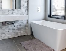 Modern bathroom with a white bathtub and brick wall.