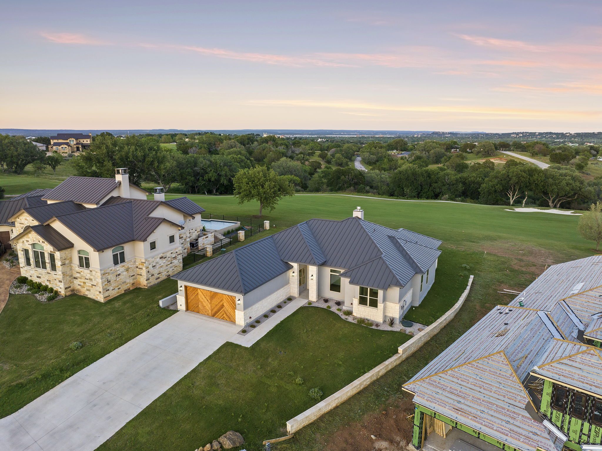 A modern house with a gray roof and wooden garage doors at sunset.