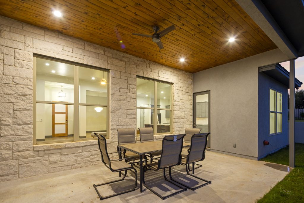 Cozy outdoor patio with table and chairs under wooden ceiling.