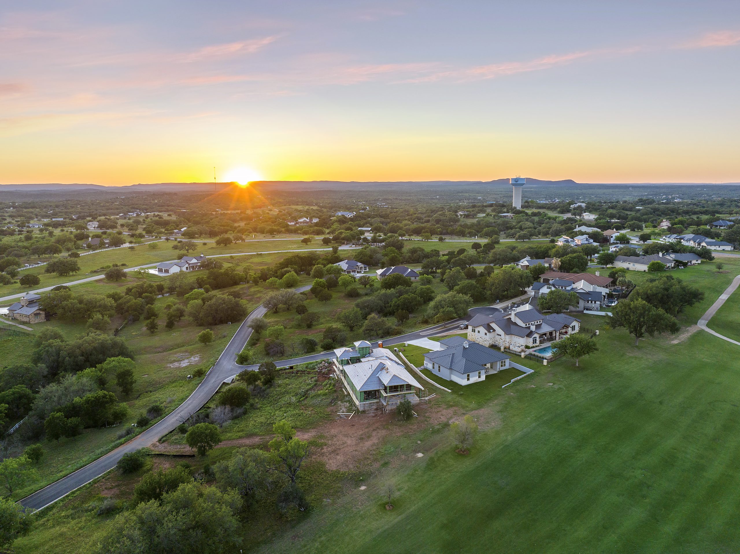 Aerial view of a golf course at sunset with houses nearby.