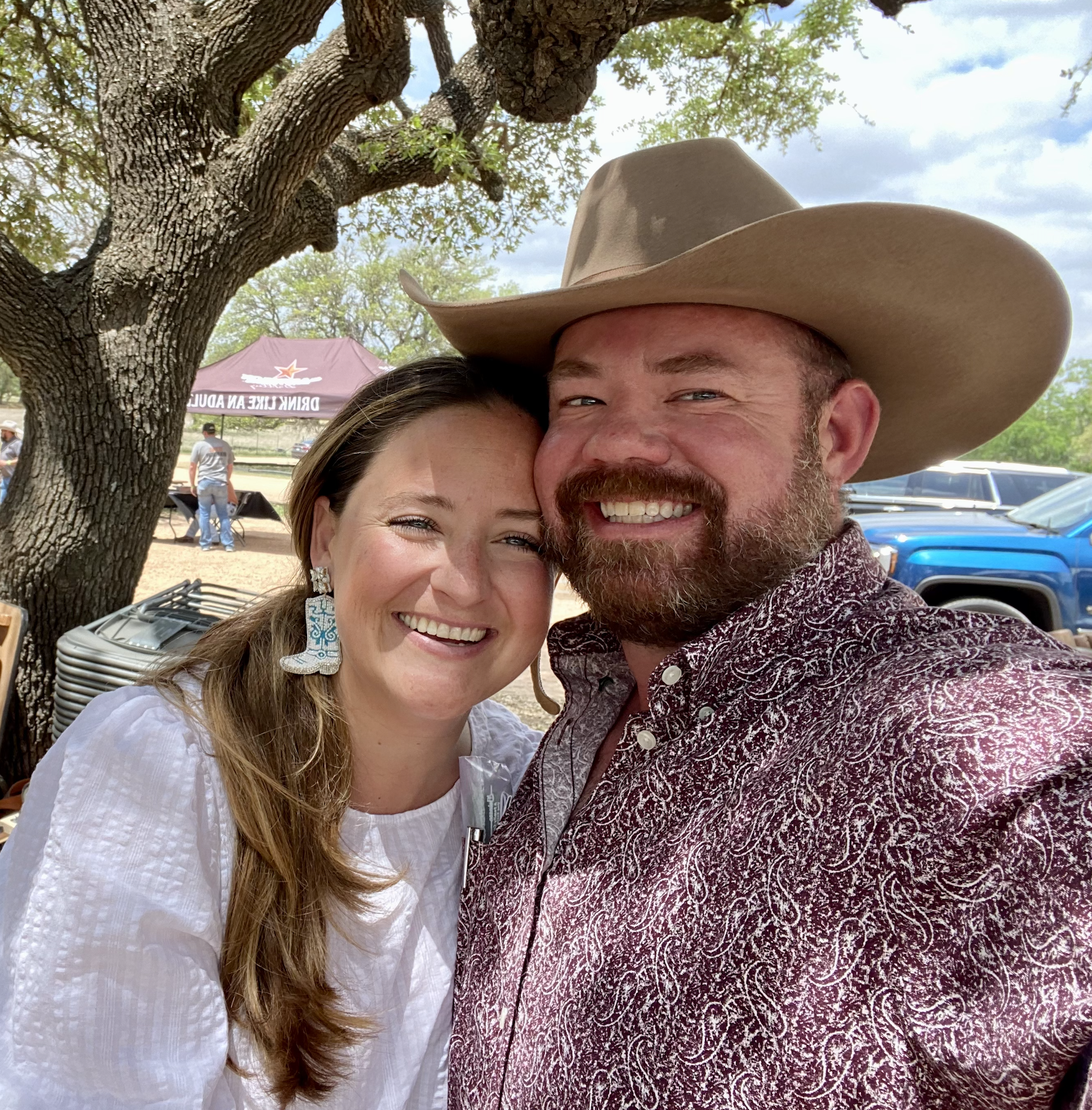A smiling couple outdoors, with the man wearing a cowboy hat.
